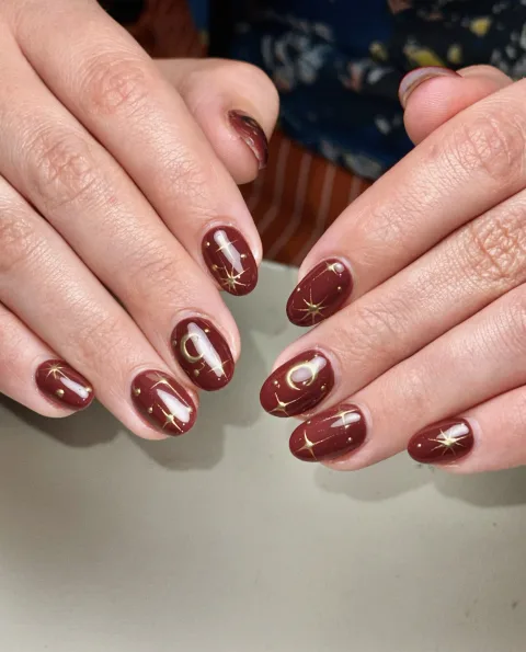 Short burgundy nails with gold stars and crescent moons