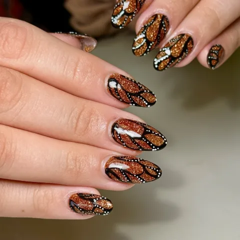 Orange glitter butterfly-wing nail art with black outlines and white dots